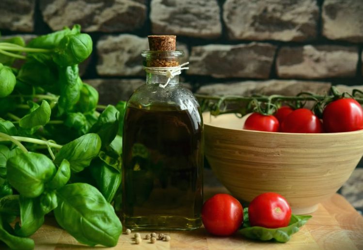 A rustic arrangement of fresh basil, ripe tomatoes, and olive oil on a wooden surface.