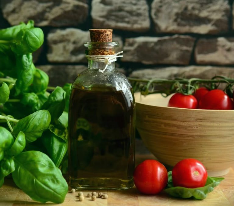 A rustic arrangement of fresh basil, ripe tomatoes, and olive oil on a wooden surface.